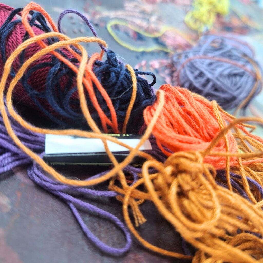 Close-up of tangled multicolored yarn skeins in purple, orange, and yellow on a dark surface.